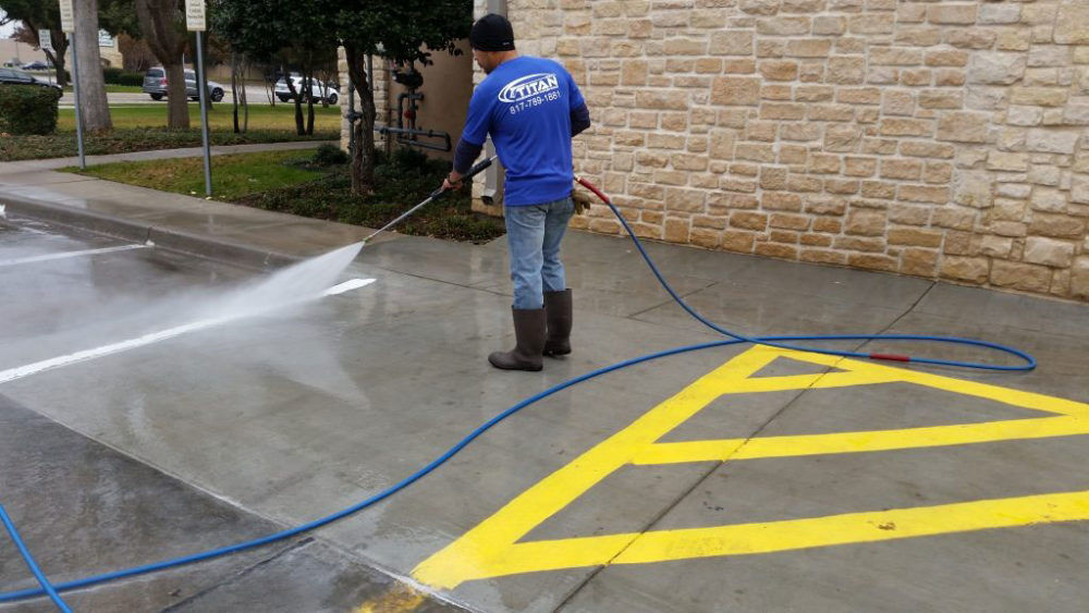 A man pressure washing the sidewalks of a restaurant in Dallas, TX